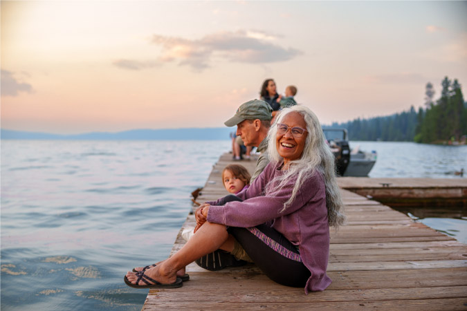 A retired woman is sitting on a dock with her son and grandchild, enjoying the view over a lake in Oregon.