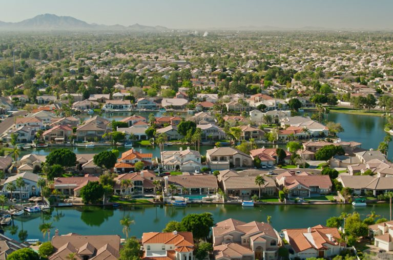 Aerial view of a residential area in the city of Gilbert, Arizona. There’s an artificial lake with rows of waterfront homes, and trees dispersed throughout the area. 