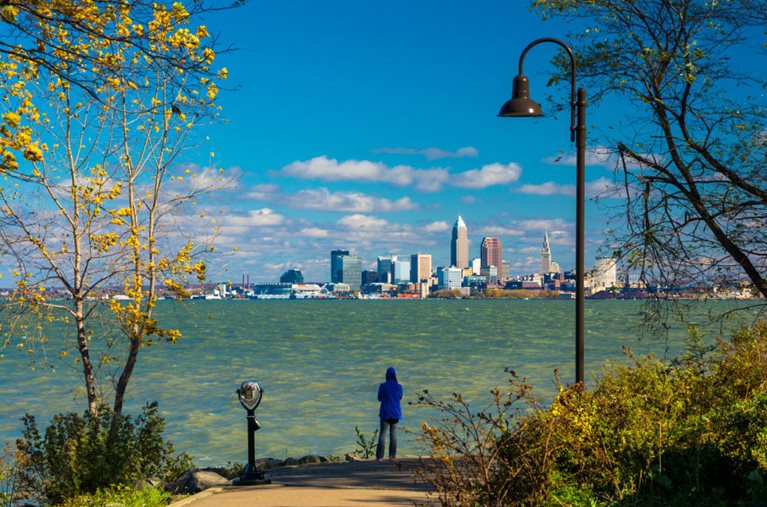A woman is looking across the water at the Cleveland, Ohio, skyline on a sunny and blustery day.