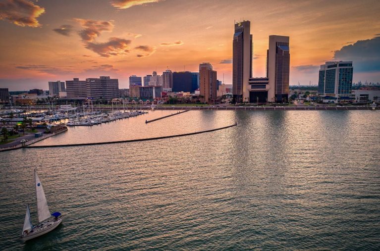 Sunset view of Corpus Christi, Texas, featuring the city skyline and a lone sailboat gliding across Corpus Christi Bay.