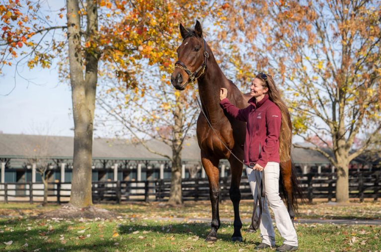 A smiling woman stands beside her horse in Lexington, Kentucky, on an autumn day.