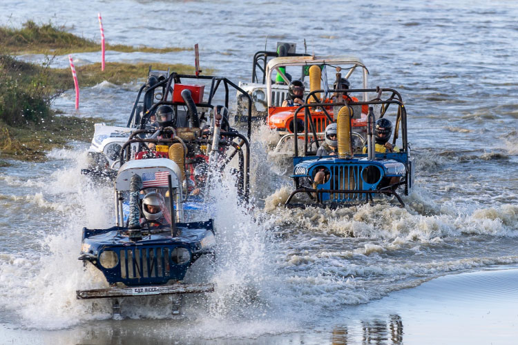 Four swamp buggies race through shallow water in Naples, Florida.  