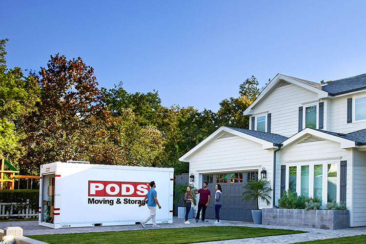 A man walks away from a PODS container sitting in his driveway, toward his family.