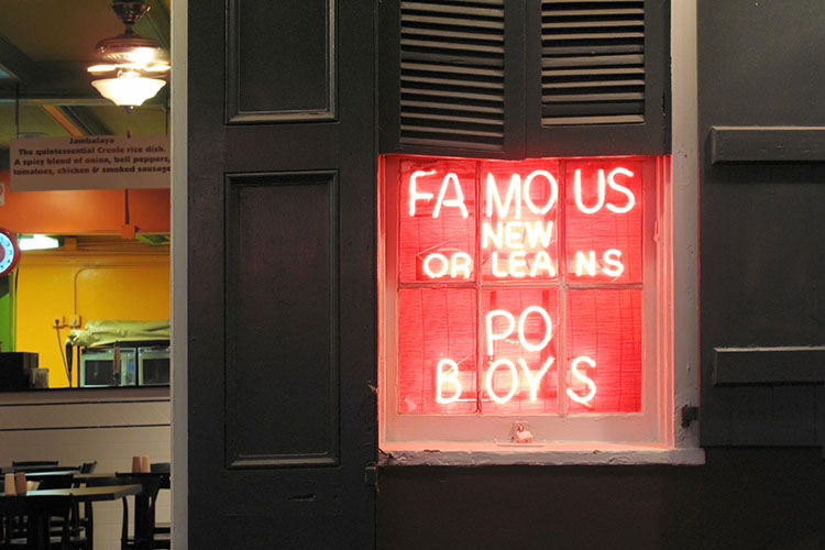 Red neon lights advertise “Famous New Orleans Po Boys” in a restaurant window