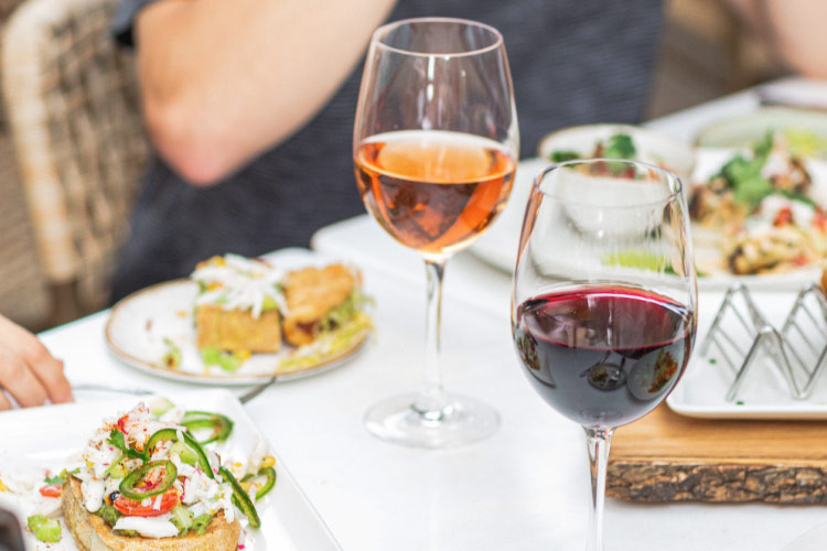 Close-up view of a dining table at The Greene House restaurant in Scottsdale, Arizona. There are various high-end fusion dishes on white plates and a couple of glasses of wine. 