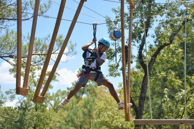 A young man is wearing a harness and safety helmet as he navigates an obstacle at Texas TreeVentures in The Woodlands, Texas.