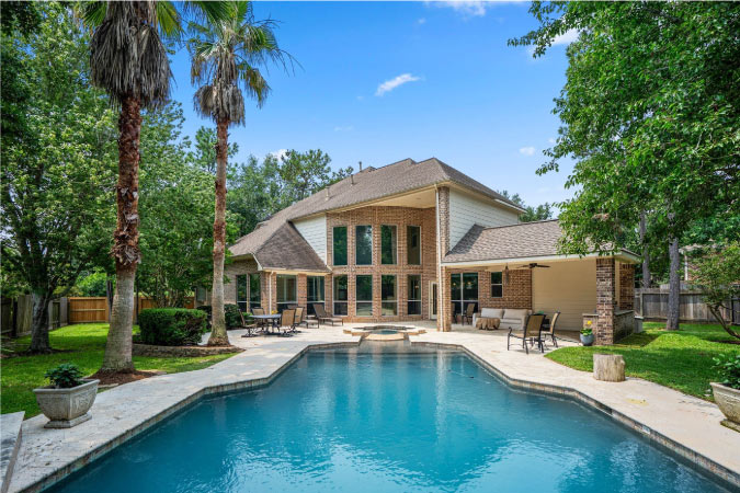 The backyard of a luxury home in the Indian Springs neighborhood of The Woodlands, Texas, features a large pool and attached hot tub. 