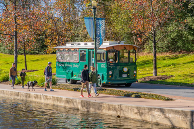 The Woodlands Town Center Trolley passes pedestrians who are strolling along a waterway in The Woodlands, Texas. 