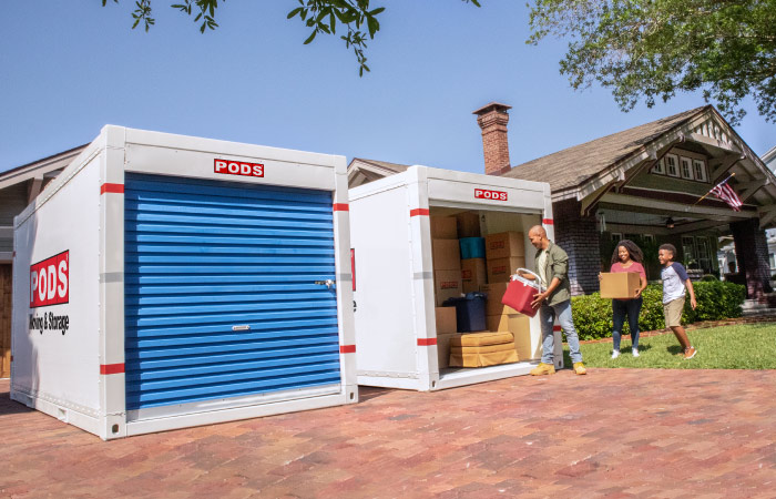 A military serviceman, in civilian clothes, and his family are loading boxes and other things into one of two PODS containers during their military move.