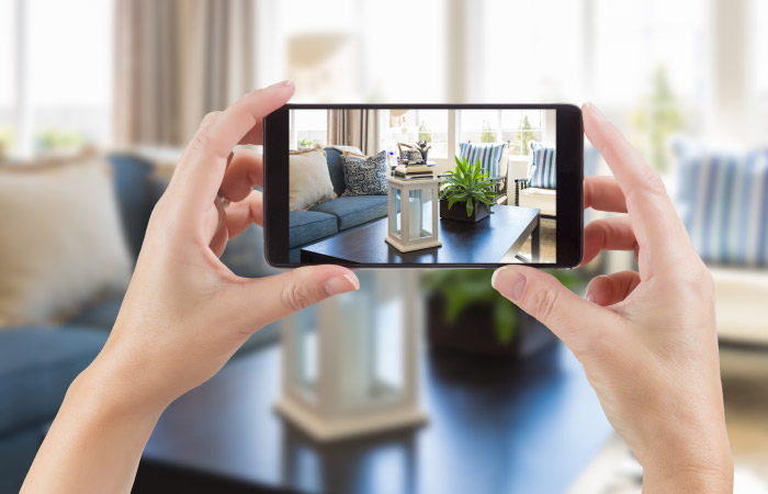 A set of hands is holding up a phone, taking a photo to document the condition of furniture and decor before military movers start packing.