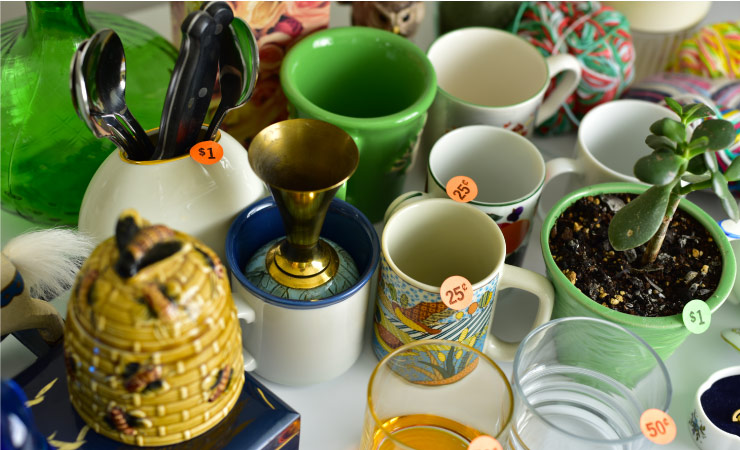 Miscellaneous dishes and other items with colorful price stickers are displayed on a table at a moving sale. 