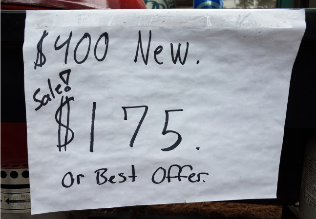 A piece of white paper is taped to an item at a moving sale. It reads, “$400 New. Sale! $175 or best offer.”