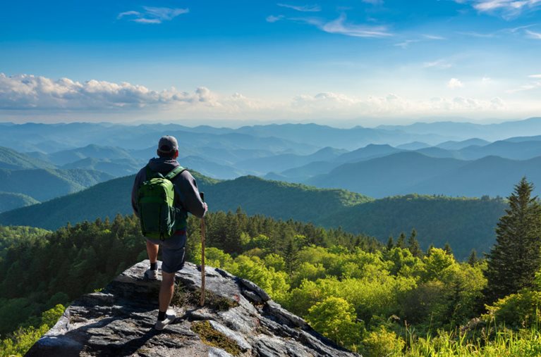 A hiker takes a break on a rocky outcrop to look out over the incredible view of the Blue Ridge Mountains near Asheville, North Carolina.
