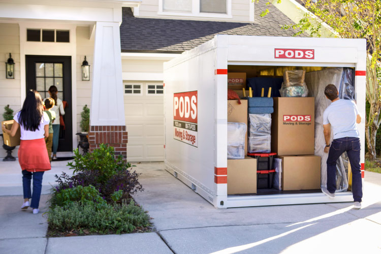 A family of four works together to unload the moving boxes and furniture from their PODS portable moving container. They’re carrying things into their new home in North Carolina.