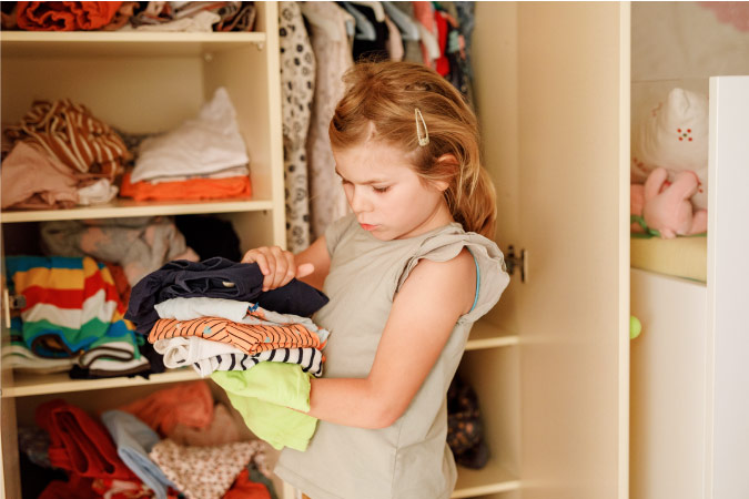 A young girl is going through her clothes while decluttering her bedroom