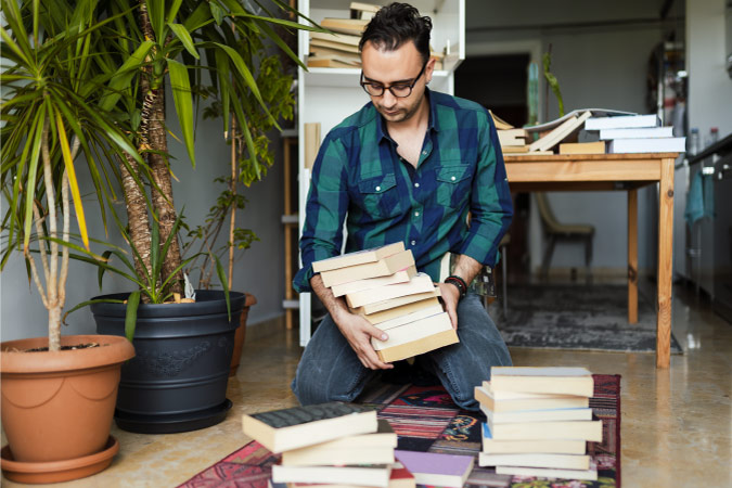 A man is going through the books in his living room to decide which to keep and which to get rid of