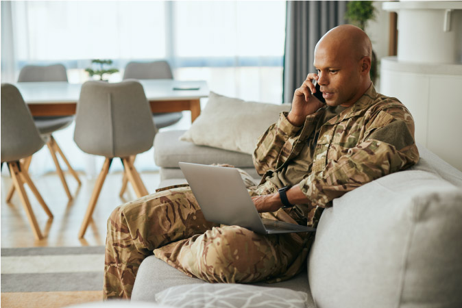 A soldier is talking on his cell phone while looking at his laptop, planning for his upcoming PCS move.