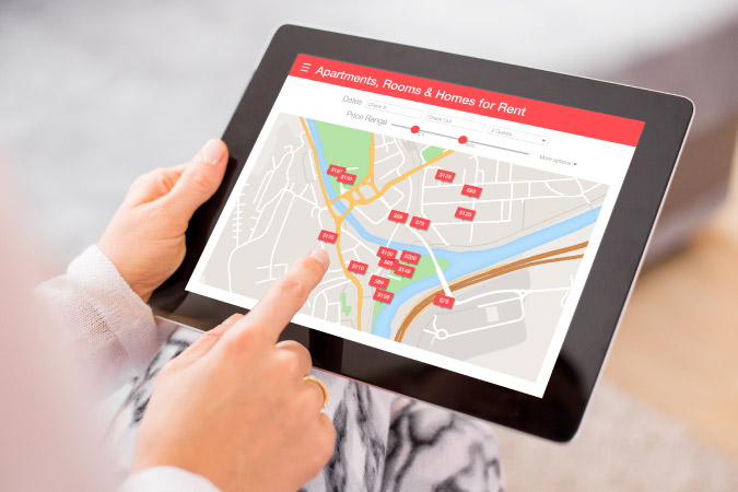 Close-up of a man’s hands as they navigate a tablet screen that’s displaying local apartments, rooms, and homes for rent.