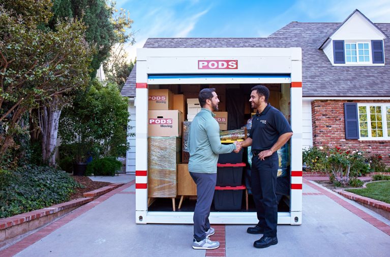 A man is smiling and shaking hands with a PODS driver in front of a fully loaded PODS portable moving container.