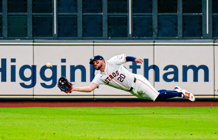 A player for the Houston Astros is leaping horizontally through the air to make a catch during a game.