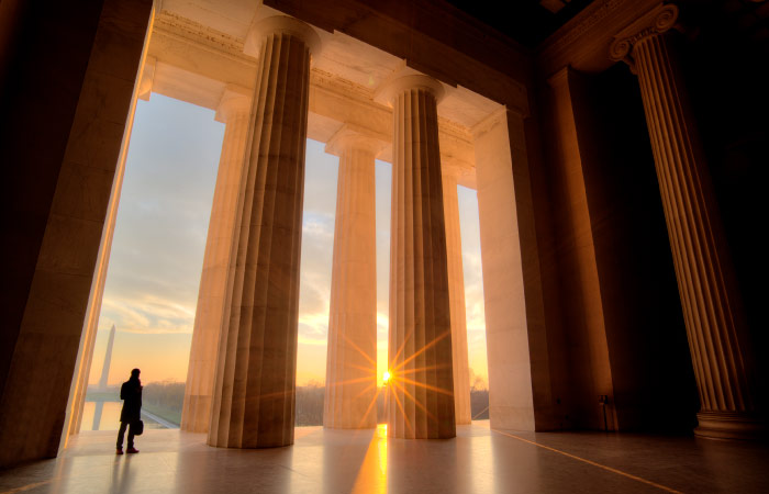 A man’s silhouette is seen between two massive columns at the entrance to the Lincoln Memorial during sunrise.