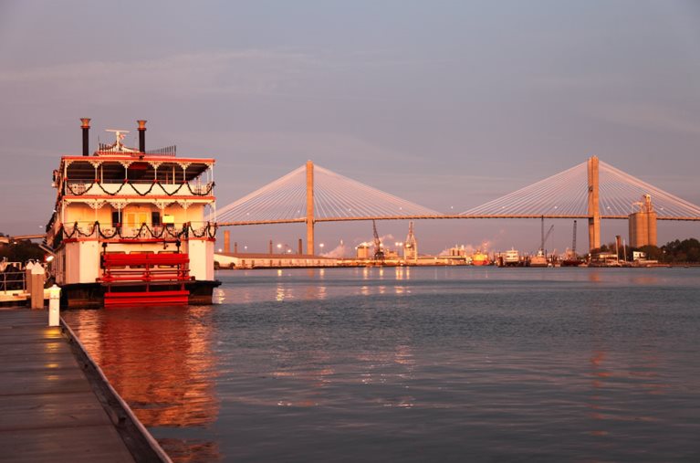 A river boat is docked in Savannah, Georgia with the Talmadge Memorial Bridge visible in the background.