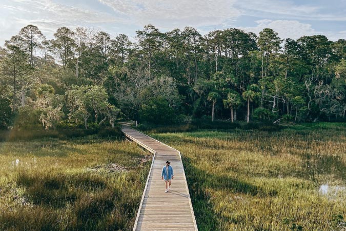 A person is walking along a long wooden boardwalk on Skidaway Island in Savanna, Georgia.