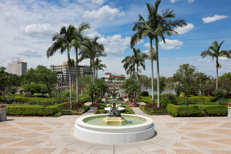 View of a water fountain and surrounding greenery in Lakeland’s Hollis Garden, with the downtown buildings visible in the distance.