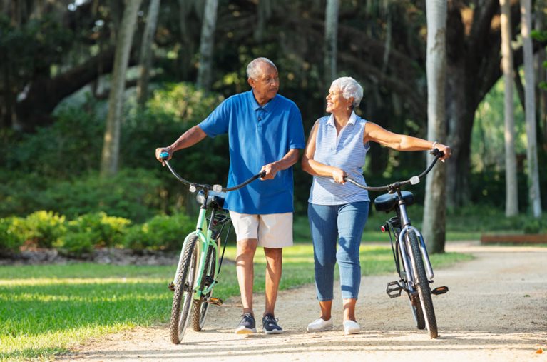 A happy couple is chatting while they walk their bikes along a sandy path in Alabama, where they recently moved for retirement.