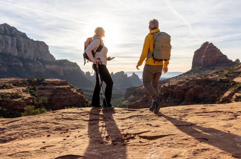 A retired couple is hiking in Arizona. They’re standing atop a rocky bluff, looking out at stunning rock formations and a deep canyon.