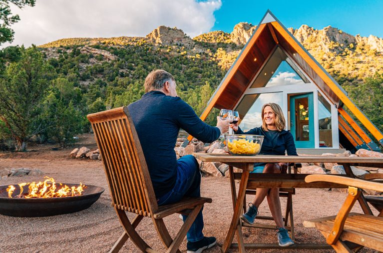 A retired couple enjoys wine with chips and salsa beside a fire pit outside their A-frame home in Colorado. 