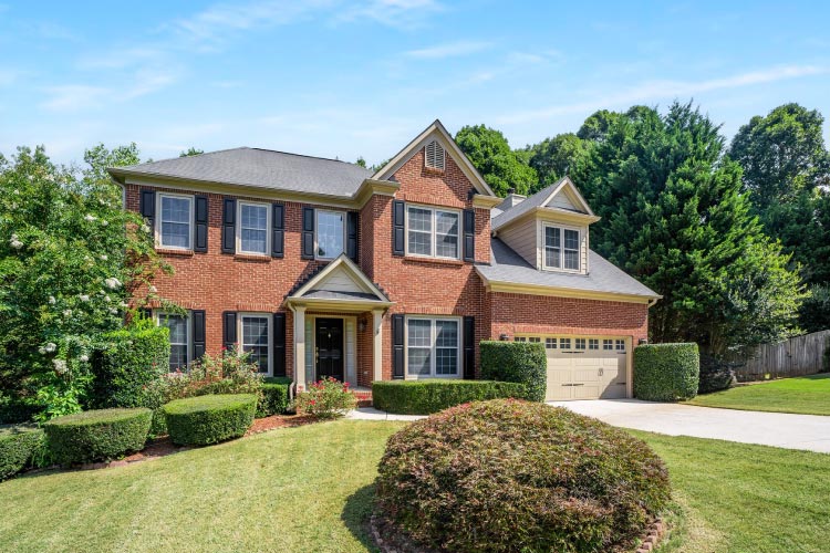 A beautiful two-story brick home nestled among a lush wooded grove in Marietta, Georgia. The home features a covered entryway, a two-car garage, and an immaculately landscaped front yard.