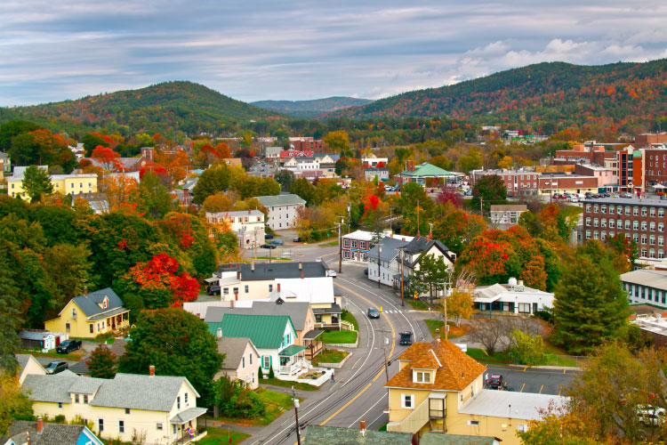 Aerial view of the town of Lebanon in New Hampshire. Rolling hills and mountains surround the town. The houses and commercial buildings of Lebanon are tucked among thick woods. 