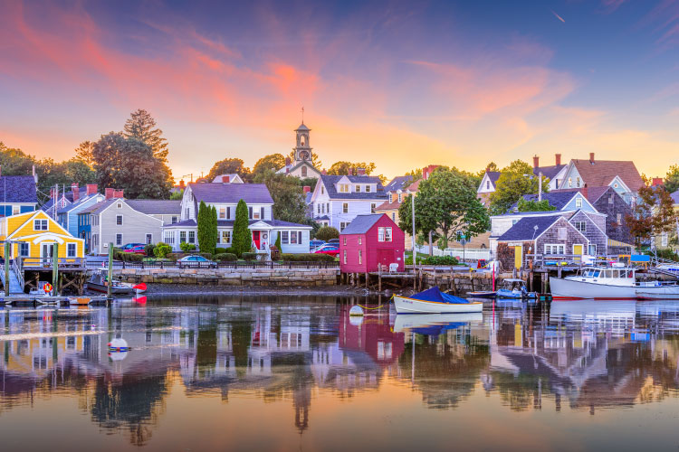 View of waterfront homes at sunset in Portsmouth, New Hampshire. The homes have a classic New England look, which is almost perfectly reflected off the calm water.
