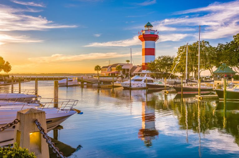 Dusk around Town Lighthouse in Hilton Head Island, South Carolina. The surrounding marina is still and quiet, and both the boats and the lighthouse are reflecting off the calm waters.