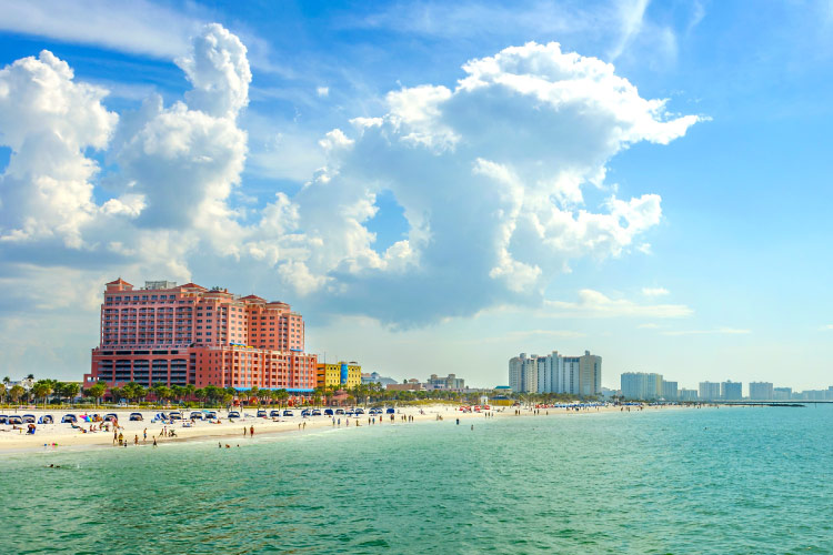 Distant view from the water of sunny and beautiful Clearwater Beach, Florida. Large colorful condo buildings and hotels dot the coast and the sugar-sand beach is filled with umbrellas and tourists enjoying the perfect summer weather. 