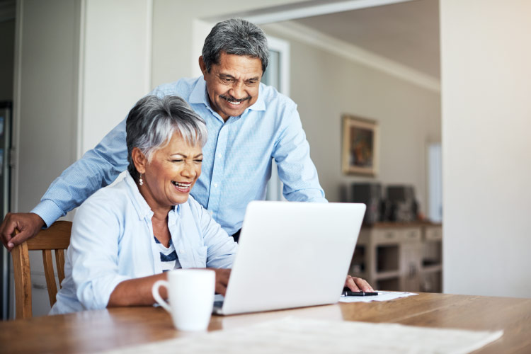 A happy older couple is using a laptop to calculate how much it will cost for them to retire in Florida. 