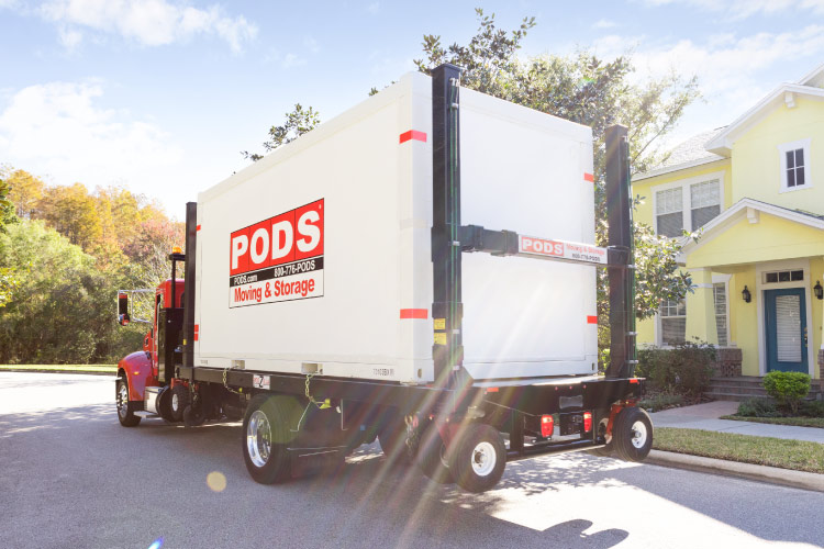 A PODS truck is transporting a PODS portable moving and storage container through a residential neighborhood toward its final destination in Florida. 