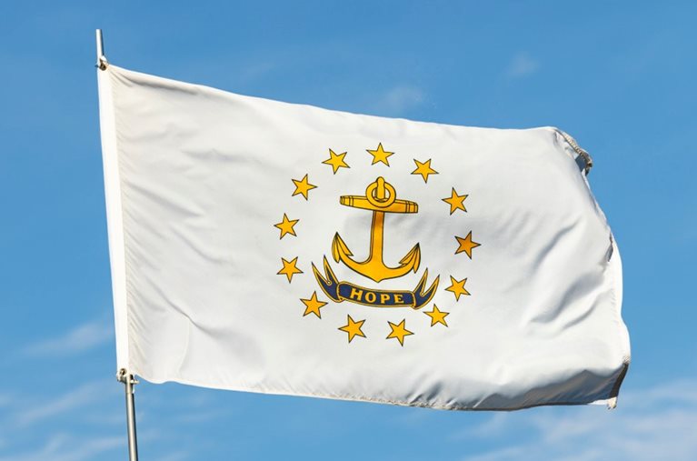 The state flag of Rhode Island, featuring a white plain with a golden anchor surrounded by golden stars. Beneath the anchor is a blue ribbon with the word “HOPE” on it.