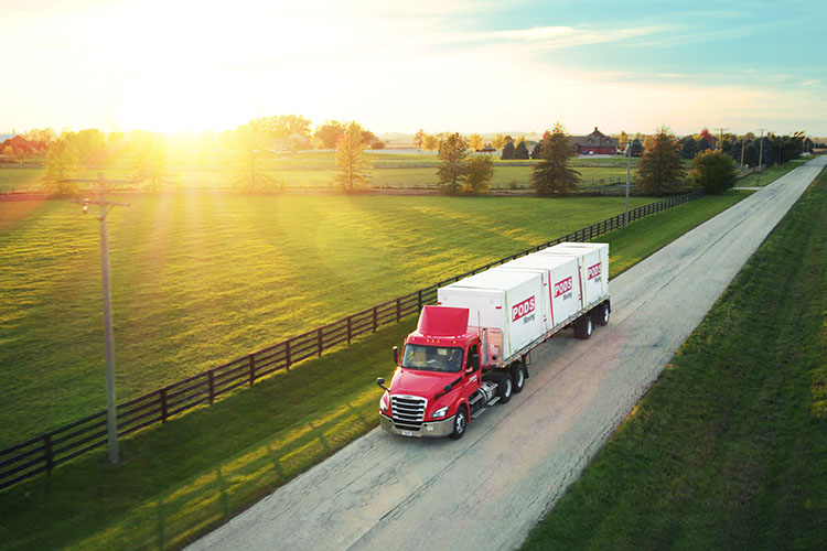 A truck with three PODS containers driving through farmland.