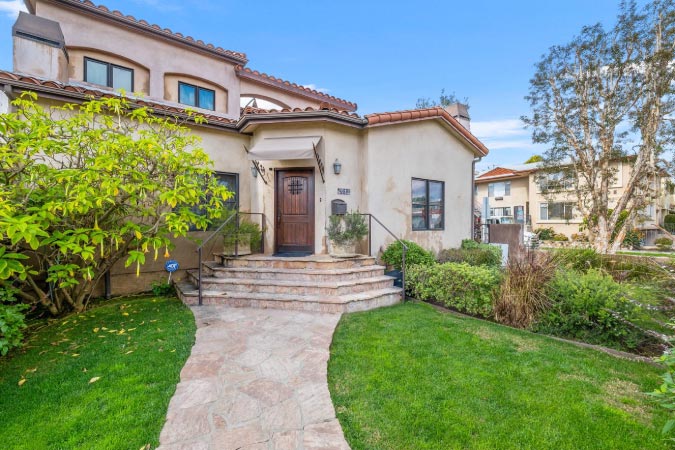 A luxurious two-story home in Beverlywood — one of the safest neighborhoods in Los Angeles — featuring a flagstone walkway and lush front yard.
