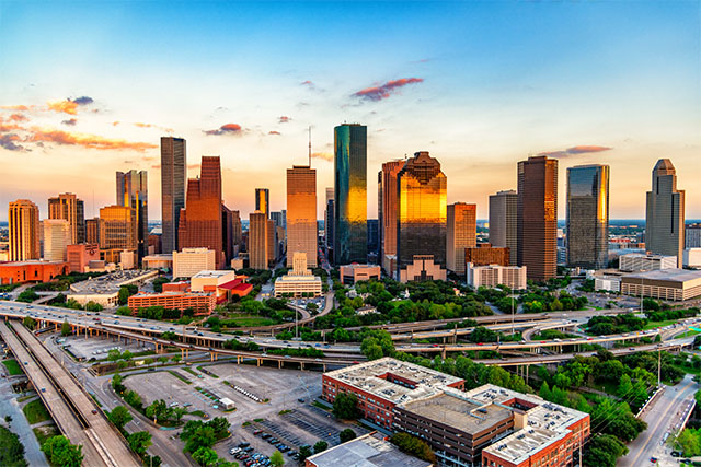 View of the Houston, Texas, skyline at sunset as the bright orange light reflects off the city’s skyscrapers.