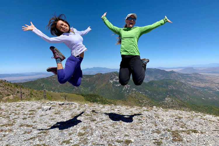 Two hikers jump for joy atop a mountain hiking trail in Sierra Vista, Arizona. 