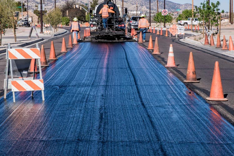 City workers apply sand seals to the road in a Sierra Vista subdivision. There are cones marking off the worksite on either side.