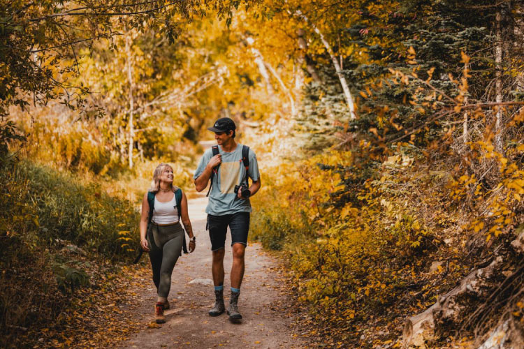 A young couple is enjoying a hike through Spearfish Canyon in Spearfish, South Dakota, on an autumn day. Some plants are still green, but the foliage on many has already turned a golden yellow.