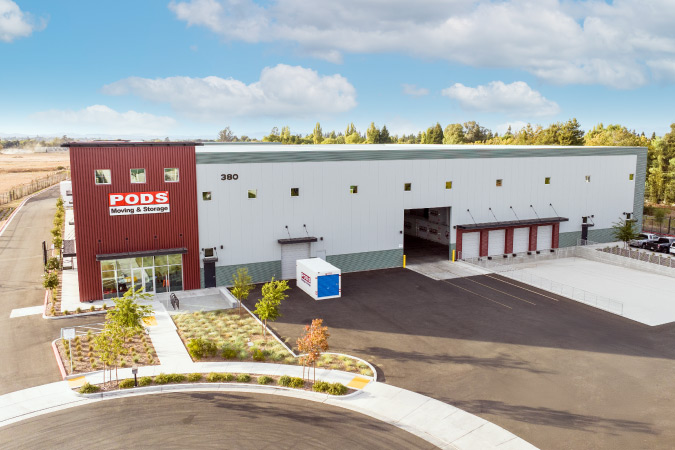Drone shot of a secure PODS Storage Center, featuring a perimeter fence and a single PODS container positioned in the front of the building.
