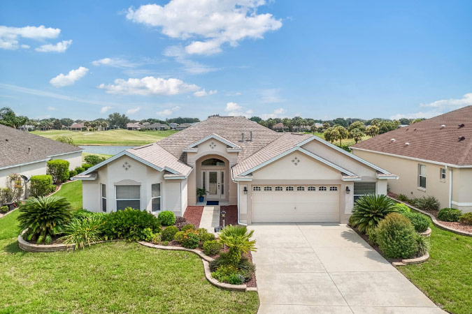 A single-family home with a green lawn and lush landscaping under a blue sky in the Village of Poinciana — one of The Villages neighborhoods in Florida.