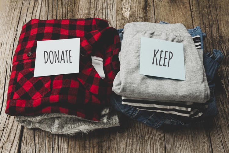 Two piles of clothing are shown on a closet floor. One has a note on top that says “donate,” and the other has a note on top that says “keep.”