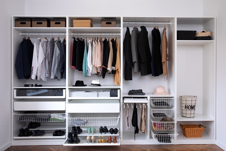 A well-organized closet system is divided into four sections. Three of the sections have a shelf on top with a clothes rod directly underneath and then more shelving and drawers below. The fourth section has shelves with various baskets stored inside.