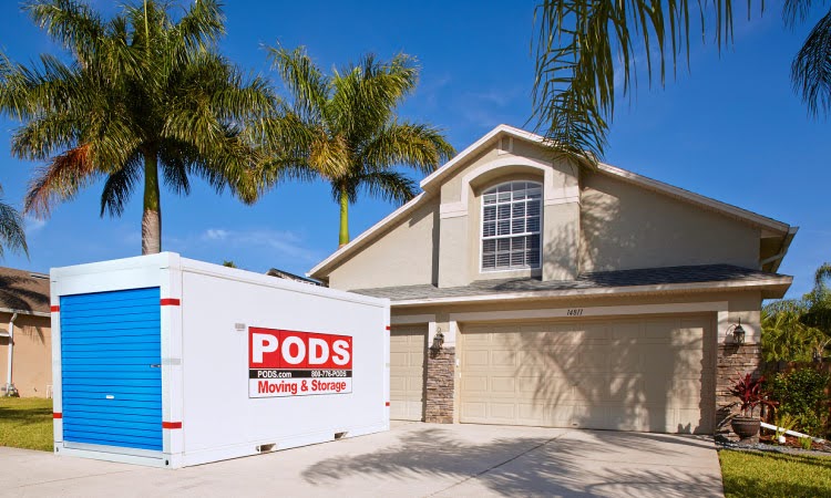 Surrounded by palm trees, a PODS portable moving container is positioned in the driveway of a classic two-story stucco home in Florida. 